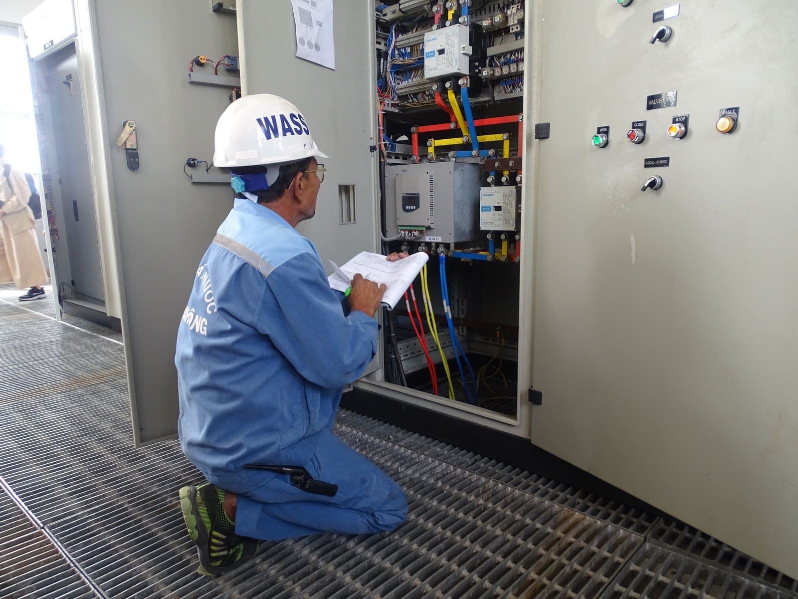 Engineer inspecting an open industrial control cabinet with PLC modules