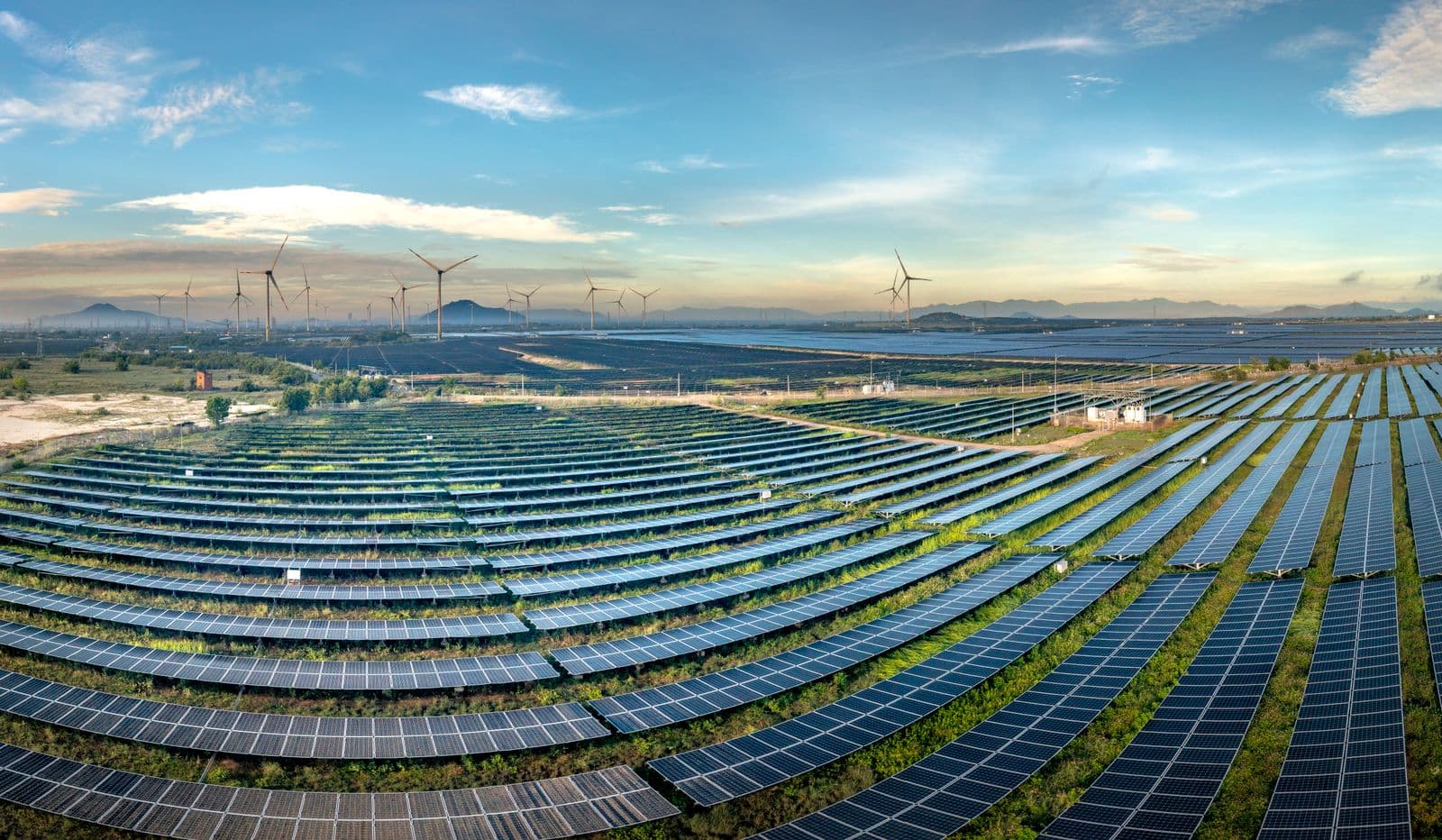 Aerial view of a solar farm with wind turbines on the horizon